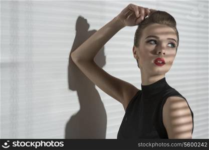 charming woman posing in creative indoor fashion shoot with elegant hairdo, stylish make-up and black dress.