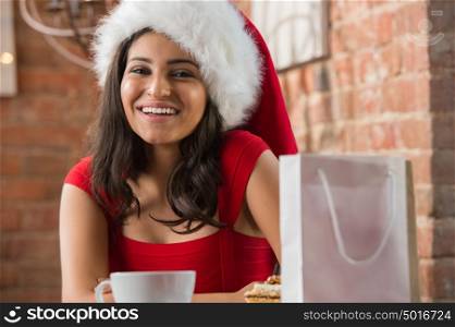 Charming woman wearing Santa Claus hat opening Christmas gift in a restaurant