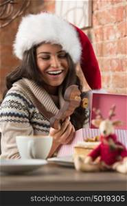 Charming woman wearing Santa Claus hat opening Christmas gift in a restaurant