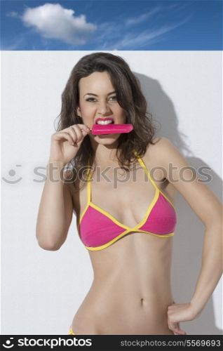 charming woman with summer style and brown curly hair wearing sexy colourful bikini and eating ice lolly
