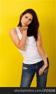 Charming young dark-haired girl in fashionable casual clothes makes posing on a bright yellow background