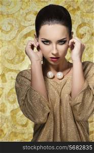 charming young female with stylish make-up wearing elegant shiny gold dress and pretty big necklace. In fashion pose