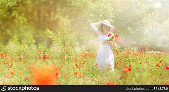 Charming young woman collects red flowers in a meadow.She is dressed in a white dress and a white hat. Small fog and sun rays