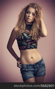 charming young woman in fashion pose with long curly hair and sexy casual style, wearing sexy top and denim short .