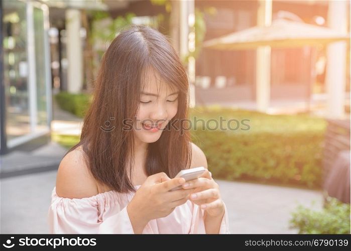 Charming young woman in white shirt reads or texts message to mobile phone, against old grunge houses in old city.