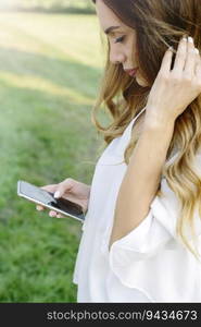 Charming young woman using mobile phone in the green park at summar day