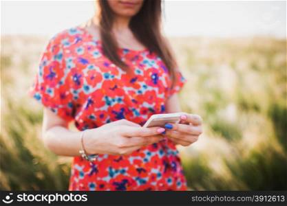 Charming young woman using to mobile smart phone, against green of summer