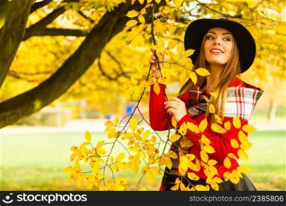 Charming young woman walking in autumnal park. Fashionable girl wearing red sweater plaid scarf and black hat.. Charming woman walking in autumnal park
