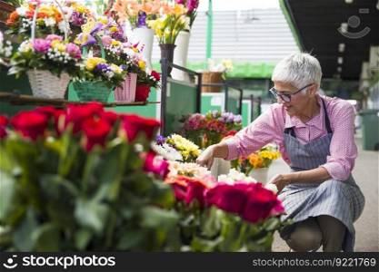 Charrming senior woman arranges flowers on local market
