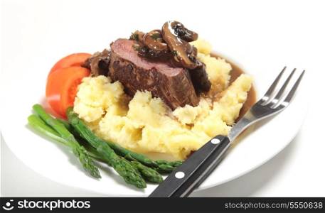 Chateaubriand beef tenderloin steak topped with a mushroom gravy sauce served on a bed of potato with asparagus and slices of tomato.