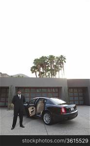 Chauffeur stands at open car door of luxury vehicle