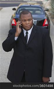 Chauffeur stands on mobile phone with luxury vehicle