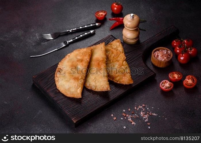 Cheburek meat pastry pie with herbs. Black concrete background. Top view. Homemade chebureks filled with minced meat and onions, traditional Caucasian cuisine