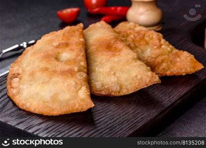 Cheburek meat pastry pie with herbs. Black concrete background. Top view. Homemade chebureks filled with minced meat and onions, traditional Caucasian cuisine