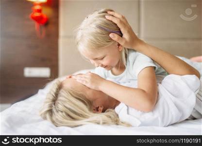 Cheeful mother and child plays hide and seek lying on the bed at home. Parent feeling, togetherness, motherhood