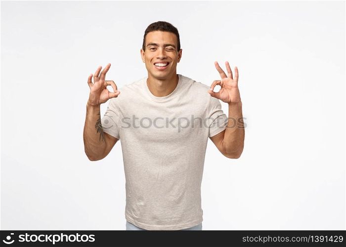 Cheeky carefree and unbothered young hispanic muscline man in t-shirt showing okay, no problem or perfect gesture, wink and smiling, encourage everything fine or excellent, recommend product.. Cheeky carefree and unbothered young hispanic muscline man in t-shirt showing okay, no problem or perfect gesture, wink and smiling, encourage everything fine or excellent, recommend product