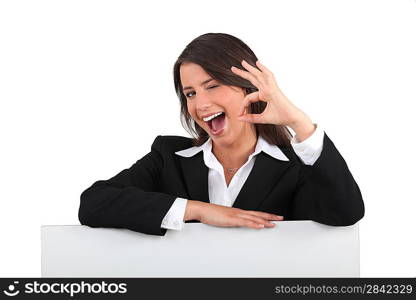 Cheeky young woman in a suit giving the OK sign with a blank board ready for text
