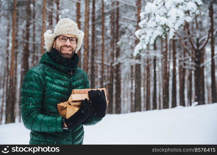 Cheerfu pleasant looking beard male model holds firewood, spends free time in forest, going to fry shish kebab, has picnic in family circle, logs wood, enjoys fresh winter forest air outdoor