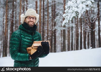 Cheerfu pleasant looking beard male model holds firewood, spends free time in forest, going to fry shish kebab, has picnic in family circle, logs wood, enjoys fresh winter forest air outdoor