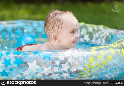 Cheerful 9 months old baby boy playing at inflatable swimming pool