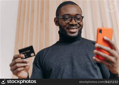 Cheerful African American businessman, credit card and smartphone, online shopping, happy smile, satisfied with successful transaction.