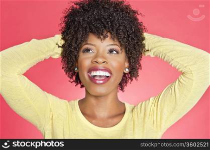 Cheerful African American looking up with hands behind head over colored background