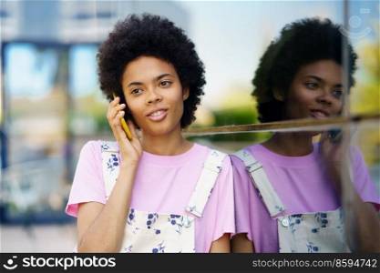 Cheerful African American woman smiling talking on her smartphone in casual clothes. Happy young female in urban background.. African American woman smiling talking on her smartphone in casual clothes.