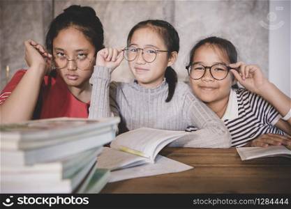 cheerful asian teenager wearing eye glasses with school book in home living room