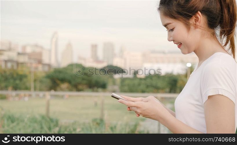 Cheerful Asian tourist blogger woman using touchscreen technology at smartphone while walking on the street at downtown city in the evening. Lifestyle backpack tourist travel holiday concept.