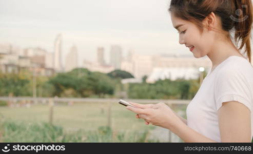 Cheerful Asian tourist blogger woman using touchscreen technology at smartphone while walking on the street at downtown city in the evening. Lifestyle backpack tourist travel holiday concept.