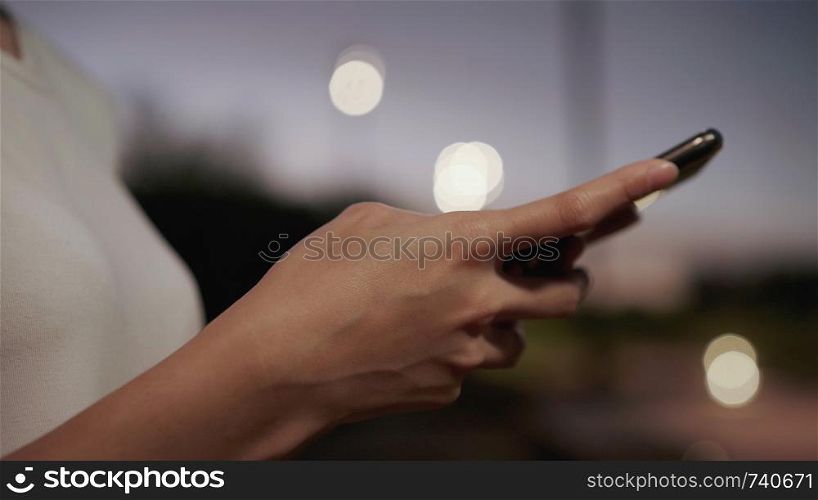Cheerful Asian tourist blogger woman using touchscreen technology at smartphone while walking on the street at downtown city in the night. Lifestyle backpack tourist travel holiday concept.