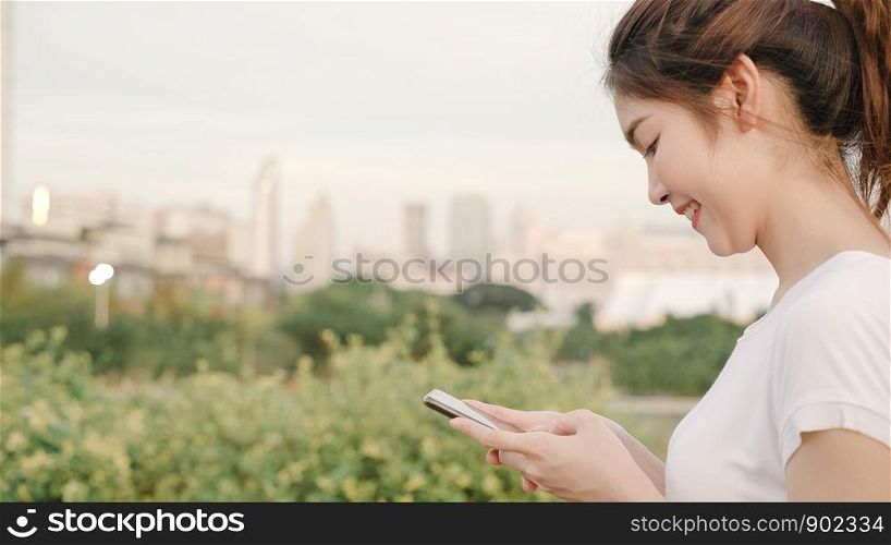Cheerful Asian tourist blogger woman using touchscreen technology at smartphone while walking on the street at downtown city in the evening. Lifestyle backpack tourist travel holiday concept.