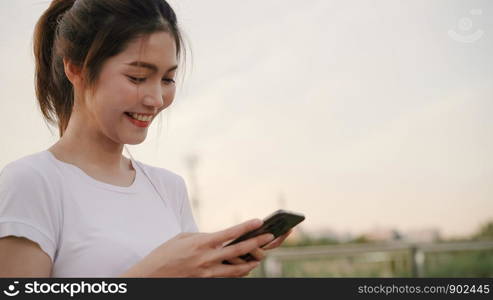 Cheerful Asian tourist blogger woman using touchscreen technology at smartphone while walking on the street at downtown city in the evening. Lifestyle backpack tourist travel holiday concept.