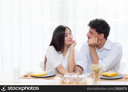 Cheerful asian young man and woman having sitting lunch and talking together at kitchen