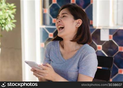 Cheerful asian young woman sitting in cafe using smartphone for . Cheerful asian young woman sitting in cafe using smartphone for talking, reading and texting. Attractive asian woman looking on her phone. Women lifestyle concept.