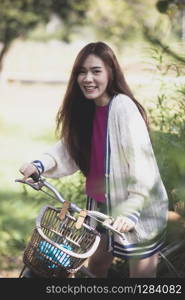 cheerful asian younger woman riding on retro bicycle in green park