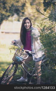 cheerful asian younger woman riding on retro bicycle in green park