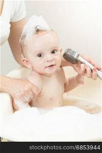 Cheerful baby boy playing with shower head in bath