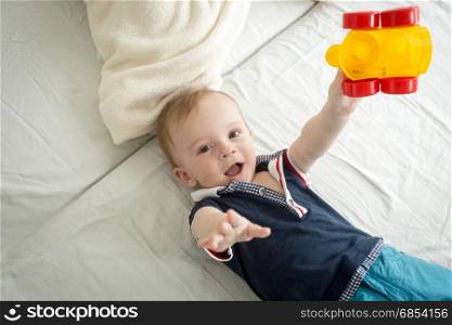 Cheerful baby boy sitting on bed and playing with toy