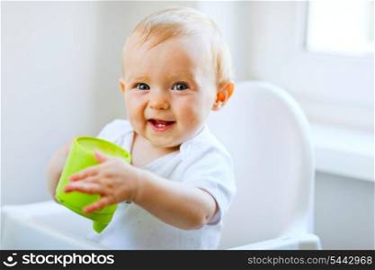 Cheerful baby girl sitting in chair and holding baby cup