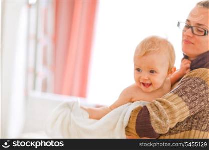 Cheerful baby on mamas arms looking in corner at home&#xA;