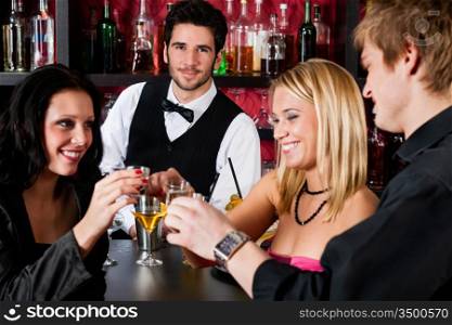 Cheerful barman behind counter with young friends at cocktail bar