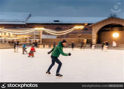 Cheerful bearded man spends Christmas time on majestic ice rink decorated with lights, skates on ice, has fun, enjoys his hobby and snowy winter weather. People, leisure, active lifestyle concept