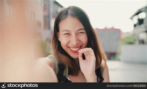 Cheerful beautiful young Asian backpacker blogger woman using smartphone taking selfie while traveling at Chinatown in Beijing, China. Lifestyle backpack tourist travel holiday concept. Point of view.