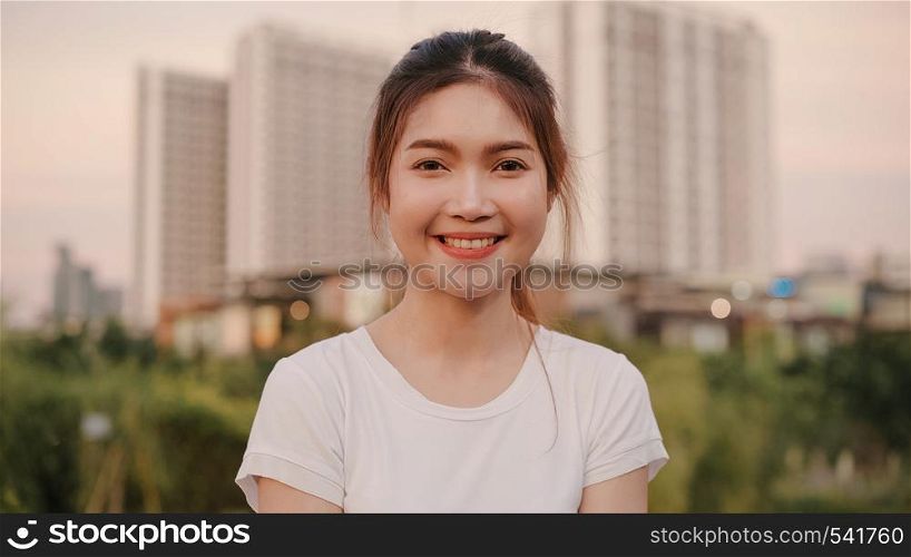 Cheerful beautiful young Asian woman feeling happy smiling to camera while traveling on street at downtown city in the evening. Lifestyle tourist travel holiday concept. Portrait looking at camera.