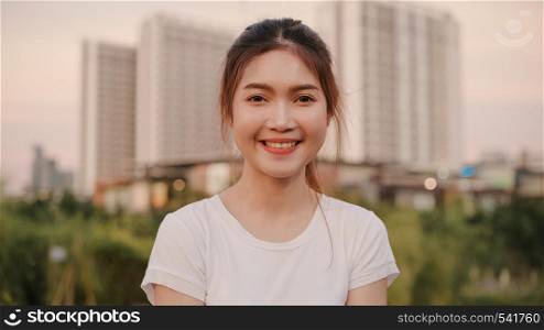 Cheerful beautiful young Asian woman feeling happy smiling to camera while traveling on street at downtown city in the evening. Lifestyle tourist travel holiday concept. Portrait looking at camera.