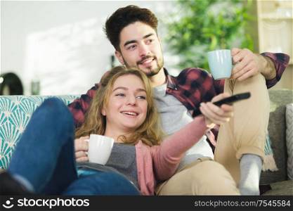 cheerful beautiful young couple drinking coffee and watching tv