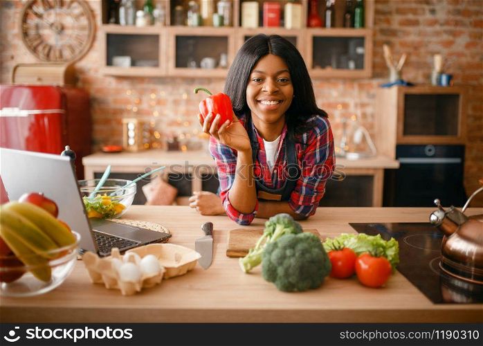 Cheerful black woman cooking healthy breakfast on the kitchen. African female person preparing vegetable salad at home
