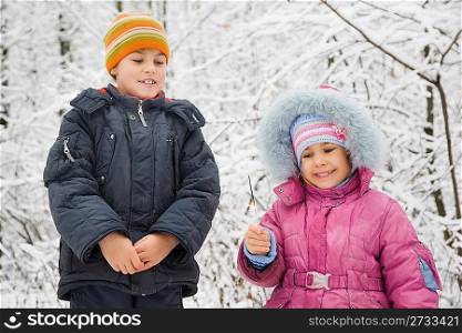 cheerful boy and little girl with Bengal fire in hand in winter in wood