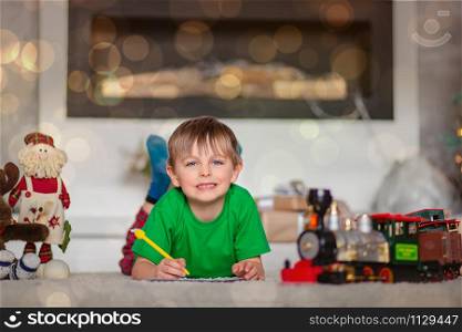 Cheerful boy is a letter to Santa, near the Christmas tree. Happy childhood, time for fulfilling wishes. Merry Christmas.. Cheerful boy is a letter to Santa, near the Christmas tree. Happy childhood, time for fulfilling wishes.